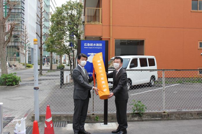 　　　仮設給水栓の寄託　　　　　　　　　　（左）飯田局長（右）穂刈理事長